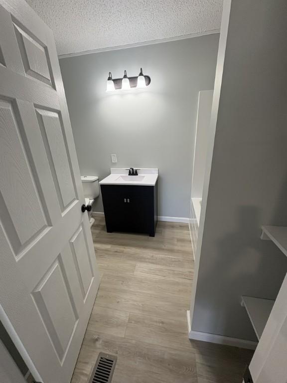 full bathroom featuring a textured ceiling, toilet, wood finished floors, vanity, and a bath