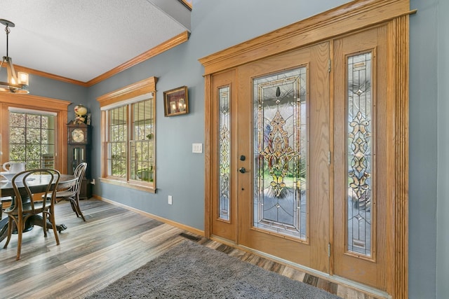 foyer entrance with wood finished floors, baseboards, crown molding, a textured ceiling, and a chandelier