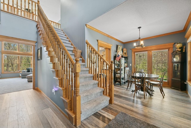 stairs with plenty of natural light, hardwood / wood-style flooring, baseboards, a textured ceiling, and crown molding