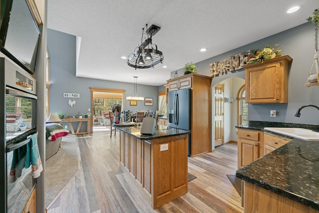 kitchen with a sink, arched walkways, light wood-style flooring, a center island, and recessed lighting
