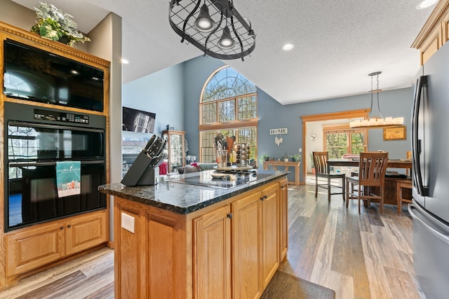 kitchen with freestanding refrigerator, cooktop, a textured ceiling, light wood-style floors, and a center island
