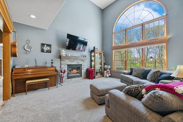 living room with a towering ceiling, carpet floors, a stone fireplace, and a textured ceiling