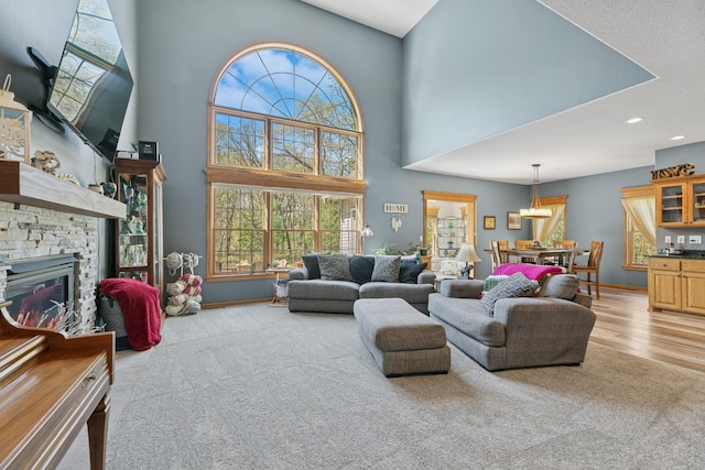 living room with healthy amount of natural light, a towering ceiling, a fireplace, wood finished floors, and recessed lighting