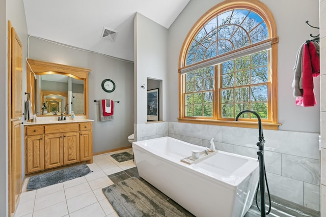 full bathroom with plenty of natural light, tile patterned flooring, a freestanding bath, vanity, and vaulted ceiling