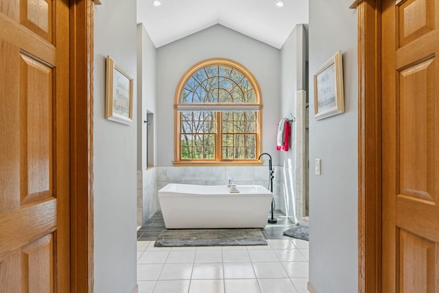 bathroom featuring tile patterned flooring, a freestanding bath, vaulted ceiling, tile walls, and wainscoting
