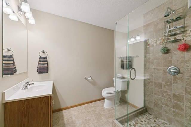 bathroom with a shower stall, toilet, vanity, a textured ceiling, and baseboards