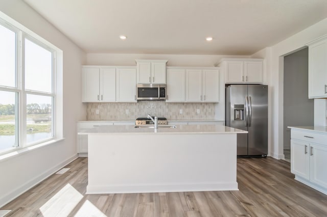 7576 Norway Ln, Lino Lakes, MN 55038 - kitchen featuring appliances with stainless steel finishes, a center island with sink, light countertops, tasteful backsplash, and white cabinetry