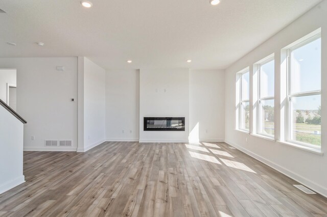 7576 Norway Ln, Lino Lakes, MN 55038 - unfurnished living room with light wood-style floors, recessed lighting, a glass covered fireplace, and baseboards