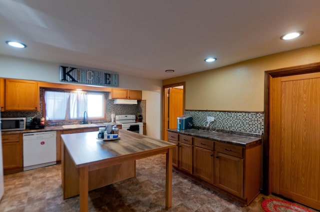 kitchen featuring white appliances, a sink, backsplash, under cabinet range hood, and recessed lighting