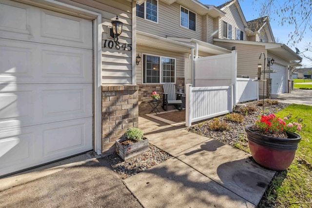 doorway to property featuring a garage, fence, stone siding, and covered porch