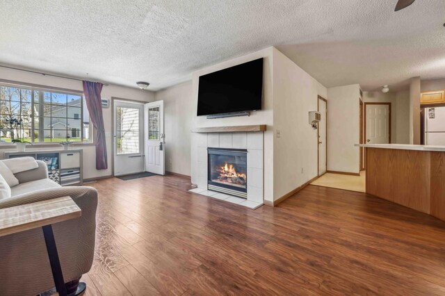 living area with a textured ceiling, wood finished floors, a tile fireplace, and baseboards