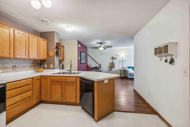 kitchen featuring black dishwasher, a peninsula, a sink, a textured ceiling, and light countertops