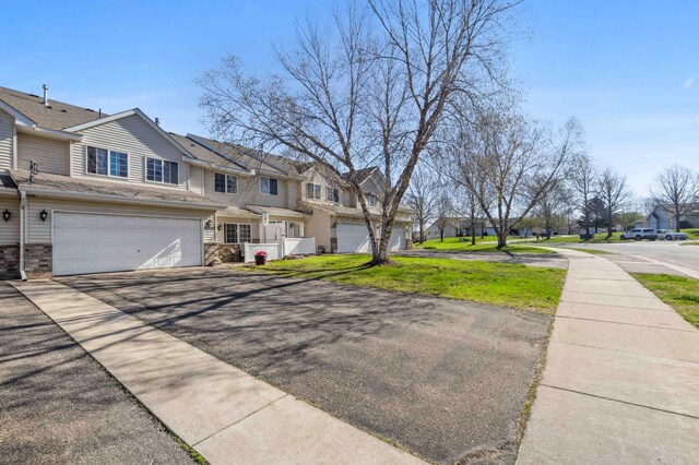 multi unit property with a residential view, asphalt driveway, a garage, and a front lawn