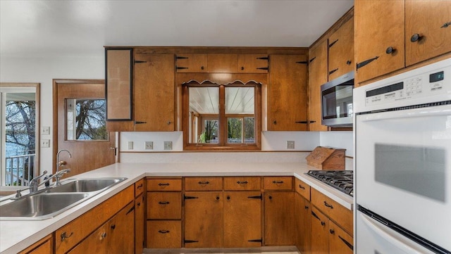 kitchen with appliances with stainless steel finishes, a sink, light countertops, and brown cabinetry