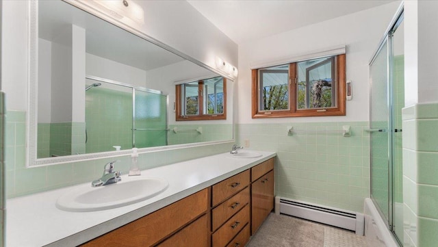 full bath featuring a baseboard radiator, tile walls, an enclosed shower, double vanity, and wainscoting