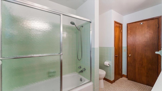 bathroom with toilet, enclosed tub / shower combo, and tile walls