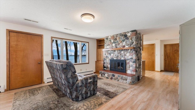 living room featuring a baseboard heating unit, light wood-type flooring, a fireplace, and a textured ceiling