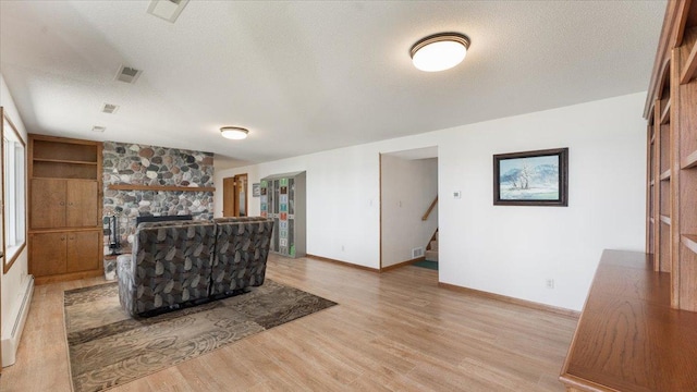 unfurnished living room with light wood finished floors, baseboards, stairs, a textured ceiling, and a stone fireplace