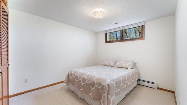 bedroom featuring a baseboard heating unit, light colored carpet, baseboards, and a textured ceiling