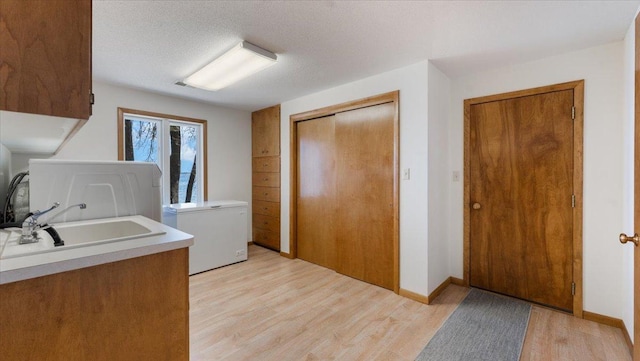 laundry area with cabinet space, light wood-type flooring, and a textured ceiling