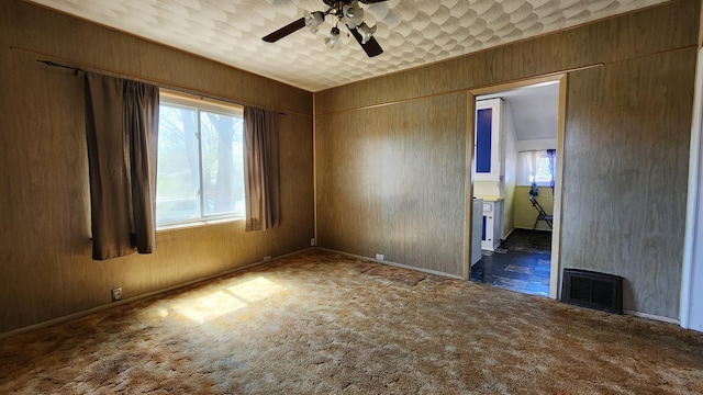 carpeted empty room featuring a ceiling fan, wood walls, and baseboards