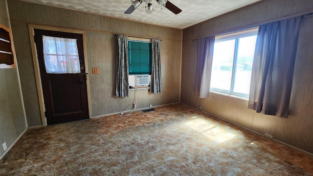 carpeted entrance foyer with wooden walls, cooling unit, a ceiling fan, and baseboards