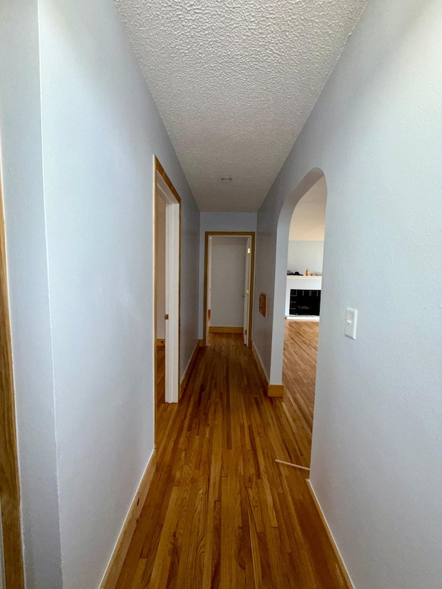 corridor featuring baseboards, arched walkways, wood finished floors, and a textured ceiling