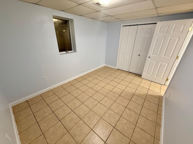 unfurnished bedroom with light tile patterned floors, a paneled ceiling, baseboards, and a closet