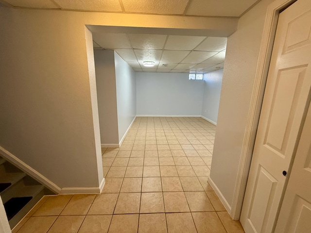 basement featuring light tile patterned floors, baseboards, and a paneled ceiling