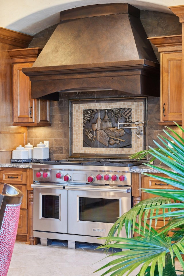 1860 Shoreline Dr, Orono, MN 55391 - kitchen with range with two ovens, decorative backsplash, brown cabinetry, light tile patterned floors, and light stone countertops