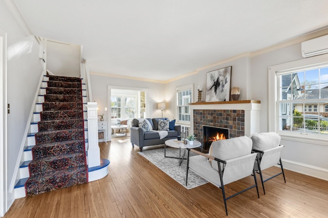 living area featuring a fireplace, an AC wall unit, ornamental molding, hardwood / wood-style flooring, and stairs