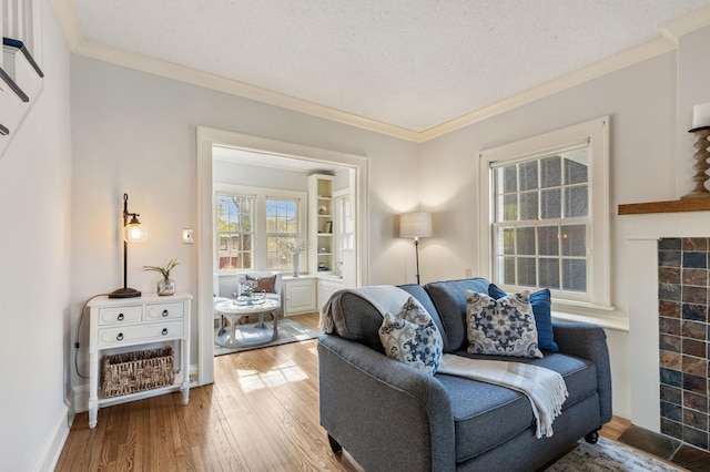 living room with crown molding, wood finished floors, baseboards, a textured ceiling, and a tile fireplace