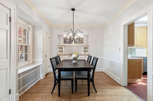 dining space with a chandelier, light wood finished floors, radiator heating unit, ornamental molding, and baseboards