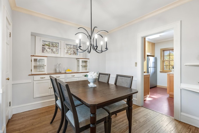 dining room featuring light wood-type flooring, crown molding, a chandelier, and baseboards
