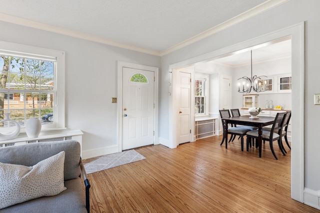 entryway with a chandelier, ornamental molding, light wood-style floors, and baseboards