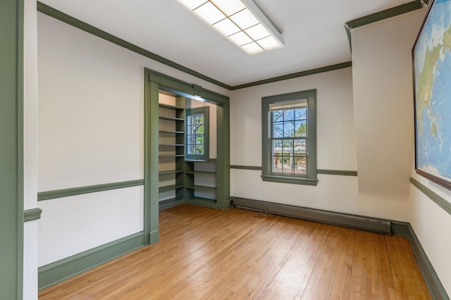 empty room featuring a baseboard heating unit, ornamental molding, light wood-style floors, and baseboards