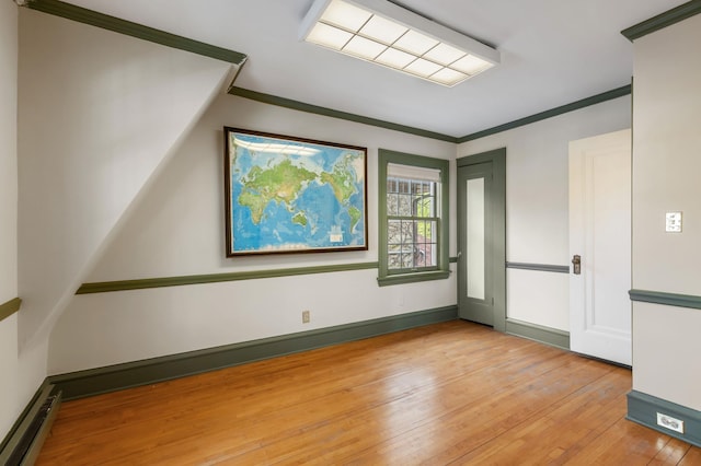 spare room with light wood-type flooring, baseboard heating, and ornamental molding