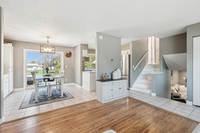 dining space with light wood finished floors, a chandelier, stairway, a textured ceiling, and baseboards