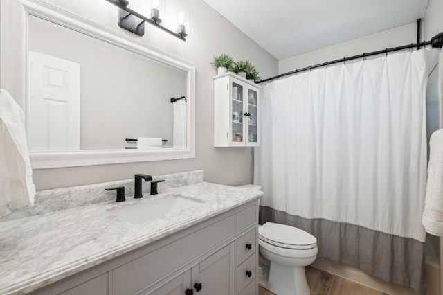 full bathroom featuring wood finished floors, toilet, vanity, a textured ceiling, and curtained shower