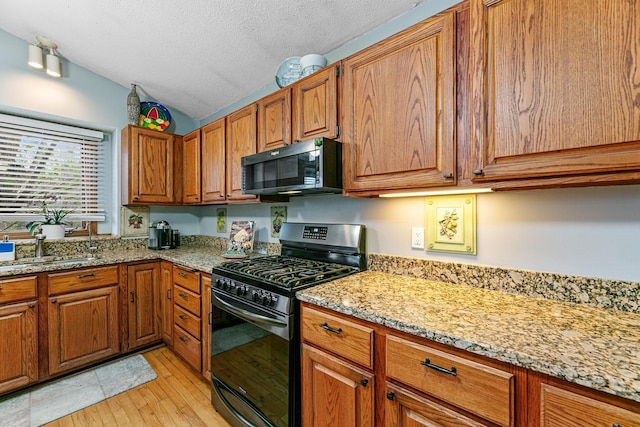 kitchen featuring black microwave, gas stove, vaulted ceiling, brown cabinetry, and a textured ceiling
