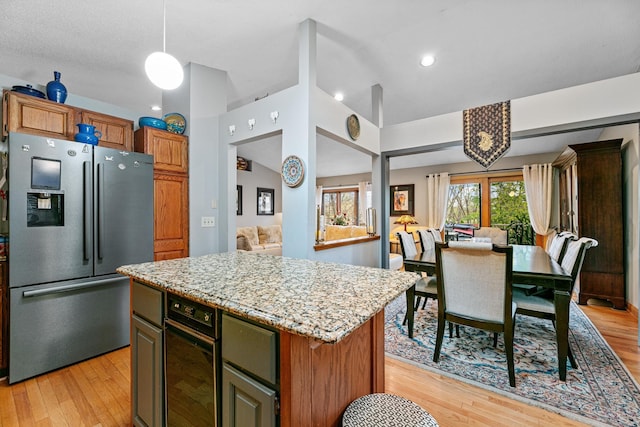 kitchen featuring stainless steel refrigerator with ice dispenser, light wood-style floors, a center island, light stone countertops, and open floor plan