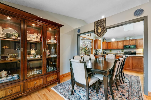 dining space featuring lofted ceiling, light wood-style floors, and baseboards