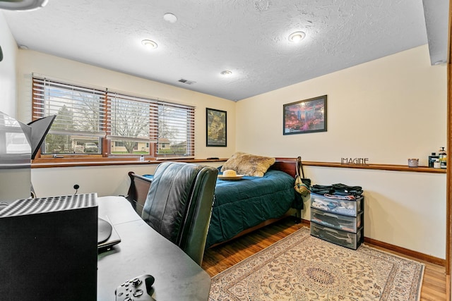 bedroom with wood finished floors, a textured ceiling, and baseboards