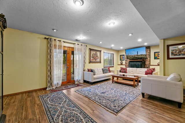 living area featuring wood finished floors, a textured ceiling, baseboards, recessed lighting, and a brick fireplace