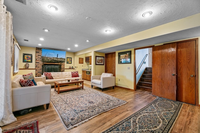 living room featuring wood finished floors, a textured ceiling, stairs, baseboards, and a fireplace