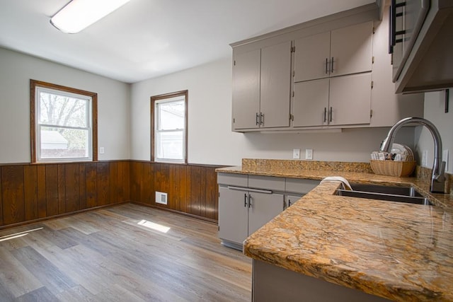 kitchen featuring a sink, a wainscoted wall, gray cabinetry, light wood finished floors, and wooden walls