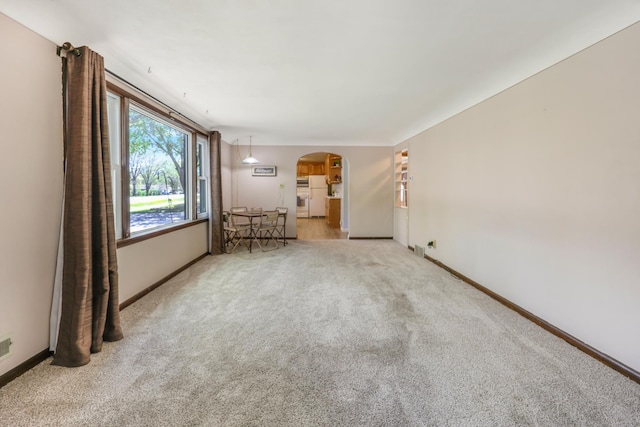 unfurnished living room with arched walkways, carpet floors, and baseboards