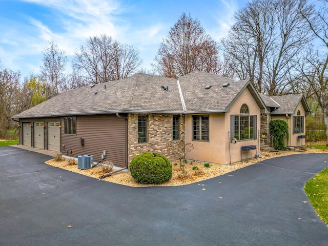 view of home's exterior with asphalt driveway, a shingled roof, a garage, and central AC
