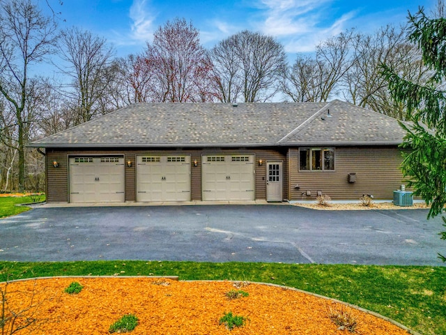 view of front of property with central AC unit, a shingled roof, and a garage