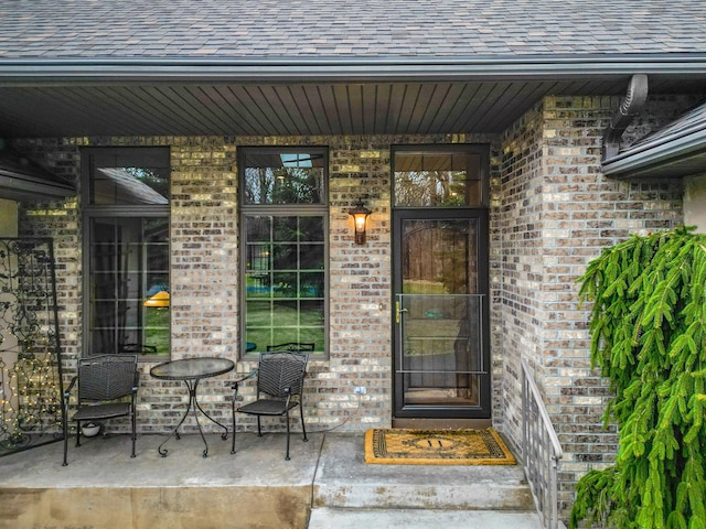 doorway to property featuring brick siding and roof with shingles